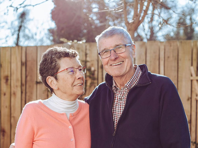 Couple smiling in garden with wooden fence in background
