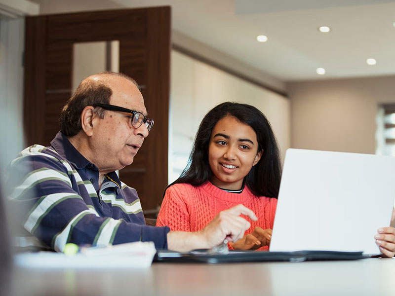 Man with glasses typing on laptop with young woman in pink jumper